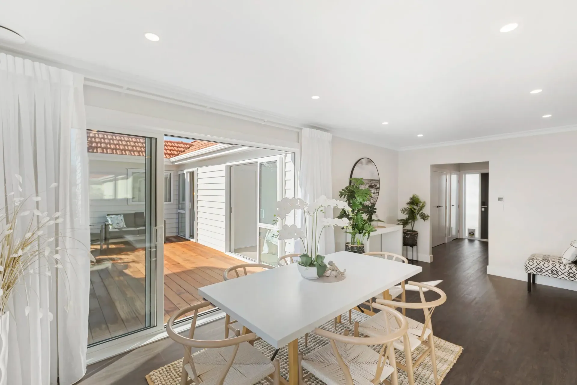 Modern dining area with a light table, wood chairs, and a sliding glass door opening to a wooden deck patio.