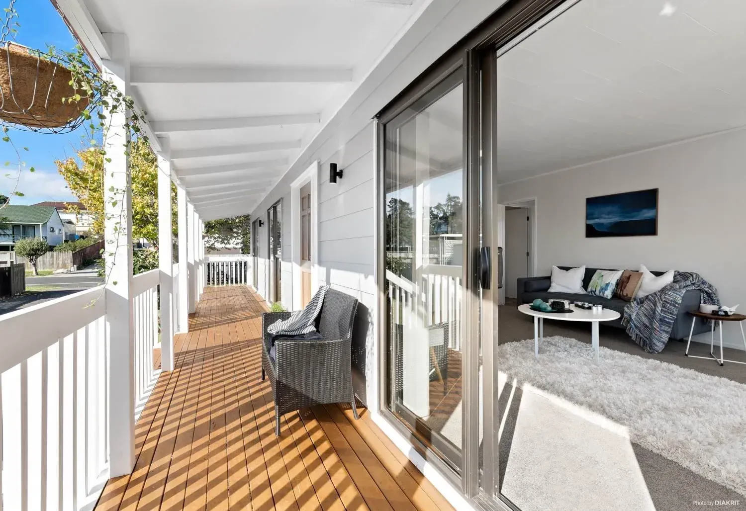A deck with wooden flooring and white railings leading to a living room with a sofa, coffee table, and area rug.