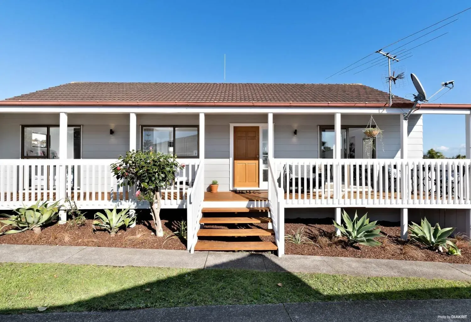 Single-story house with light grey siding, a front porch, and wooden stairs, set under a clear blue sky.