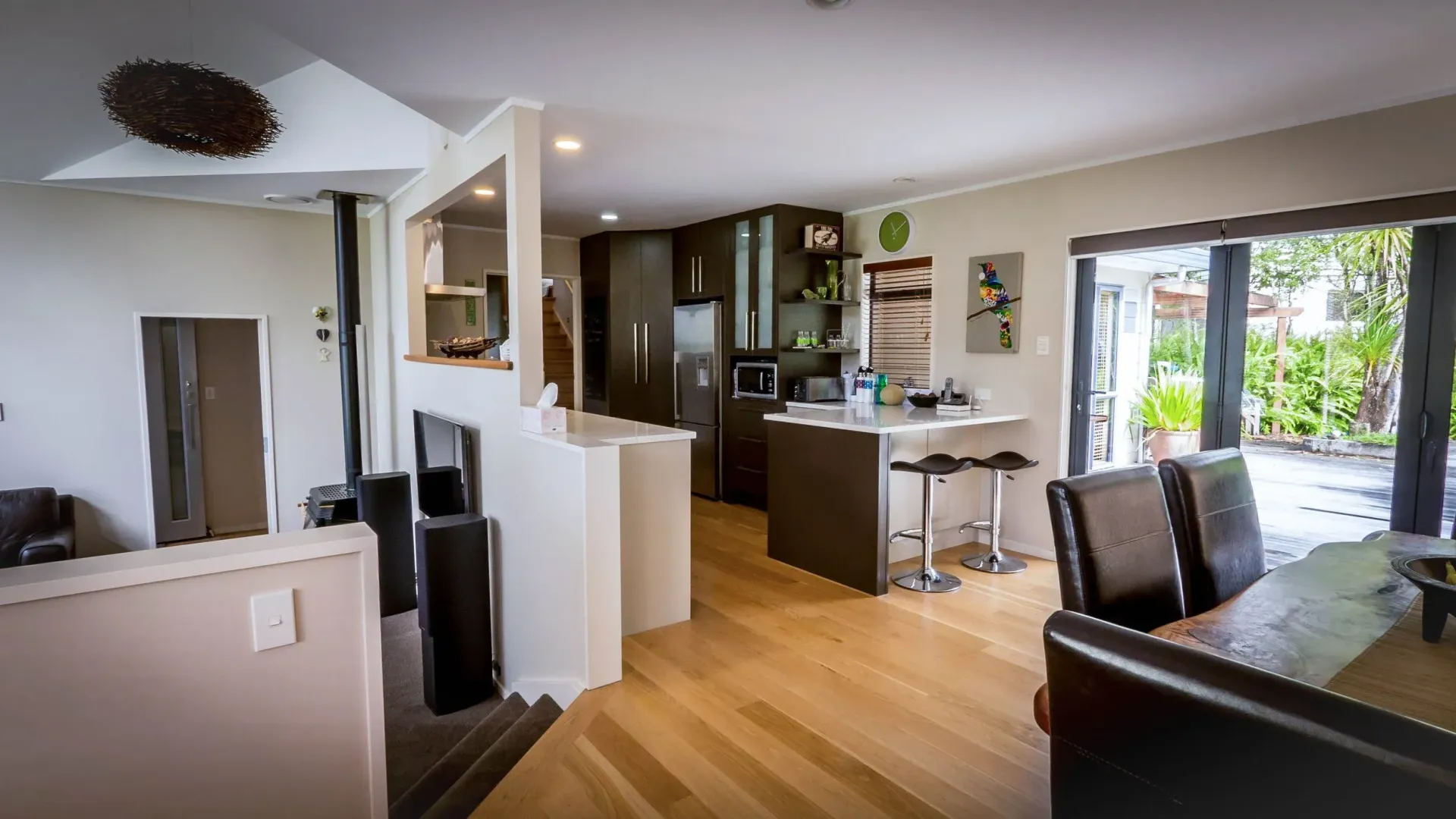 An open-plan living and dining space with light wood flooring, a central kitchen island with stools, and a patio door.