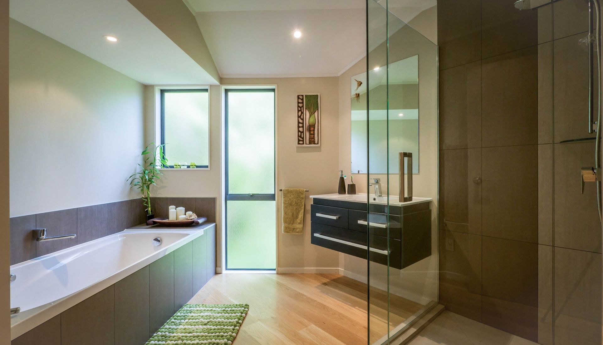 Modern bathroom with a white soaking tub, a dark floating vanity, light wood flooring, and a glass-enclosed shower.