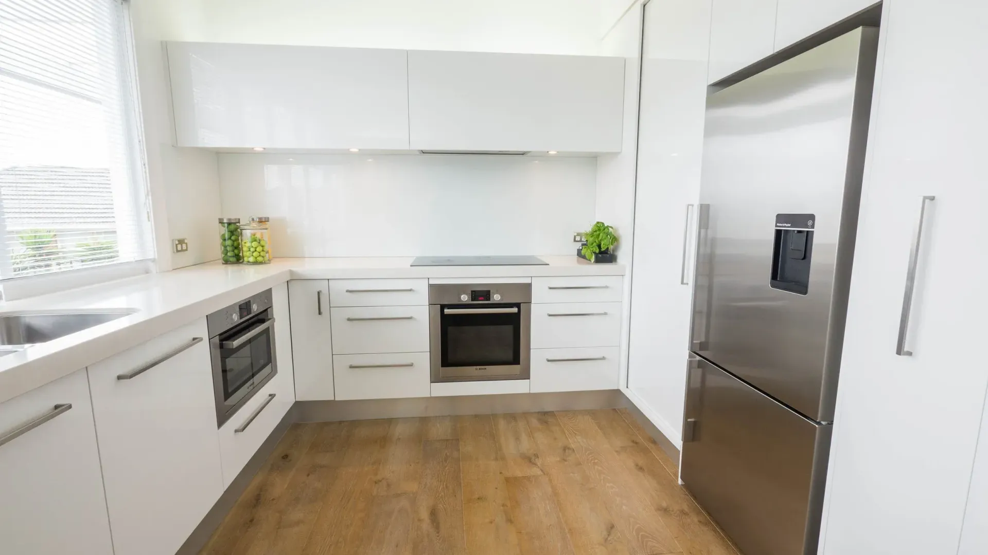 Modern kitchen with white cabinets, stainless steel appliances, and wood-look flooring.