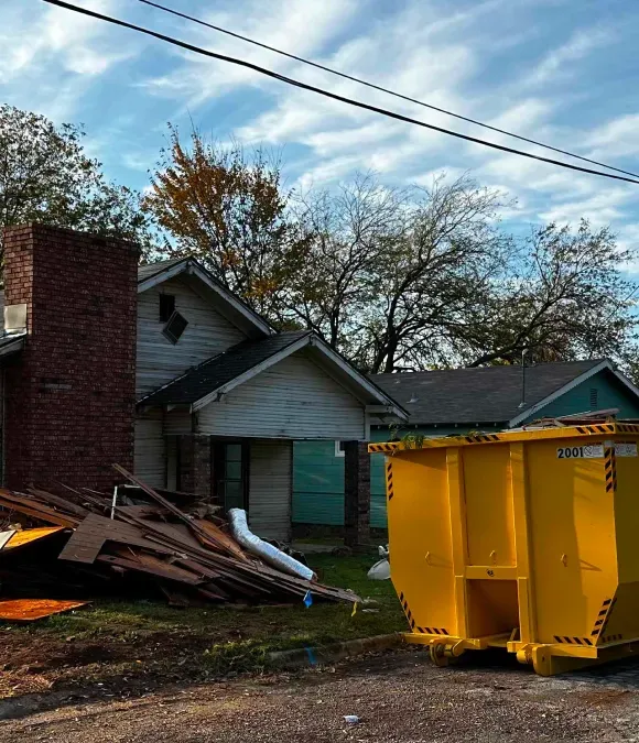 A yellow dumpster is parked in front of a house