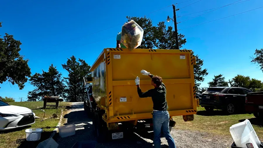 A man is standing in front of a yellow dumpster.