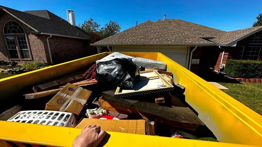 A dumpster filled with boxes and trash is in front of a house.