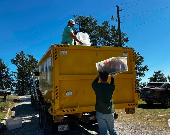 A man is loading a large plastic bag into a yellow dumpster