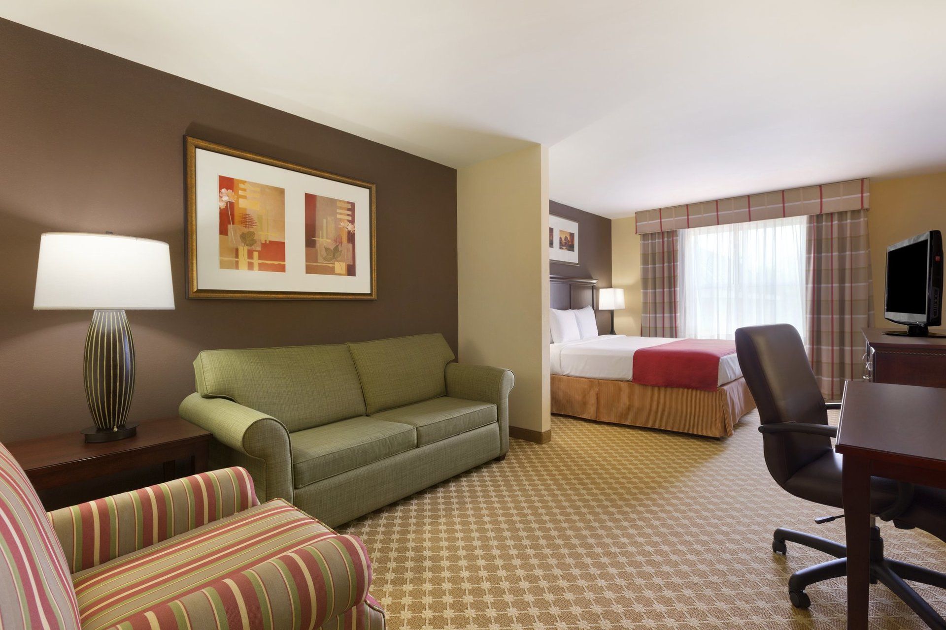 A hotel room with a couch , chair , desk and television