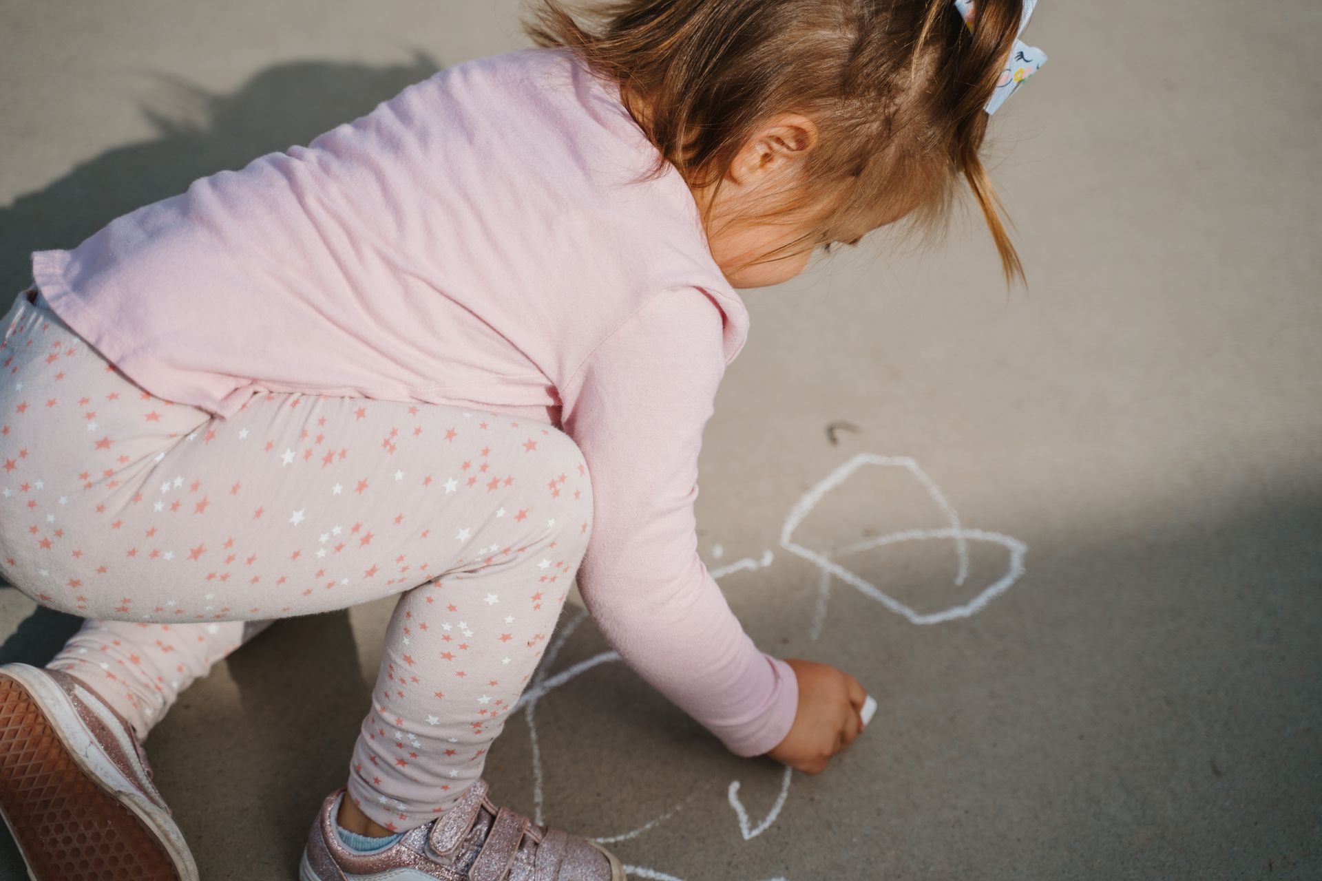 A little girl is drawing a heart with chalk on the ground