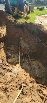 Trench excavation with exposed pipes and muddy soil beside a blue tractor.