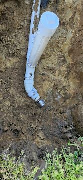 White PVC pipe protruding from a dirt trench near grass and soil.