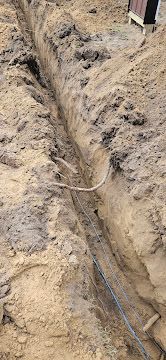 Narrow dirt trench with exposed cables running along the bottom at a construction site