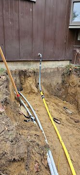 Trenched backyard with exposed utility lines and pipes beside a brown house wall