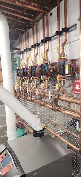 Industrial boiler room with wall-mounted pipes, gauges, valves, and a large metal unit in the foreground