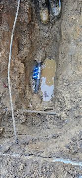 A narrow dirt trench with a blue canister and a pale patch on the soil wall.
