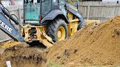 Yellow backhoe digging soil beside a large dirt pile on a construction site.