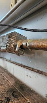 Close-up of a rusted pipe with a damaged, taped joint against a wall and floor.