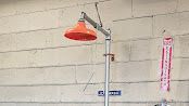 Red showerhead mounted on a pipe against a white cinderblock wall.