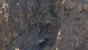 Close-up of rough dark brown rock or soil surface with a small crack and shadowed crevice