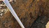 White pipe against a dirt trench wall beside a dark dug-out hole