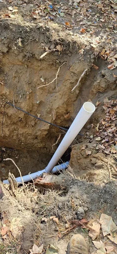 A white pipe is laying in the dirt in a hole.