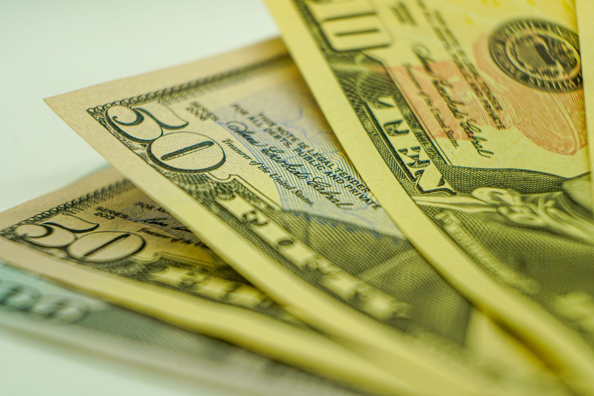 Several U.S. dollar bills fanned out on a light surface, with 20 and 100 notes visible