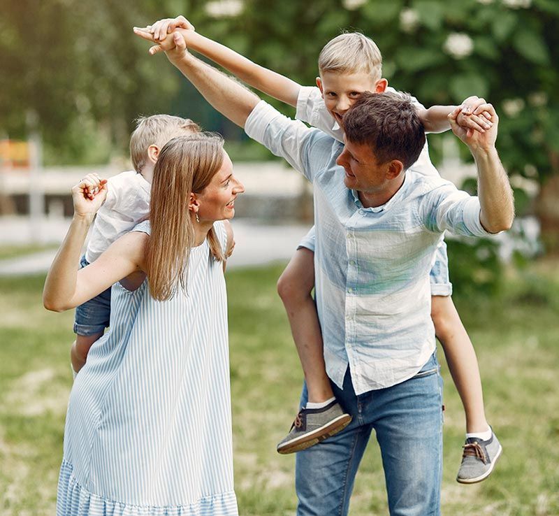A man is carrying two children on his shoulders in a park.