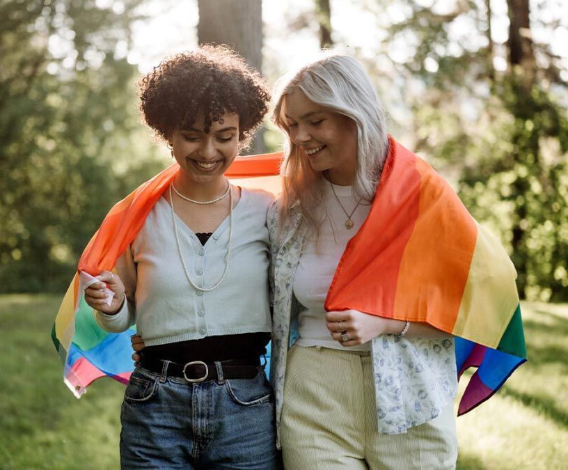 Two women are standing next to each other holding a rainbow flag.