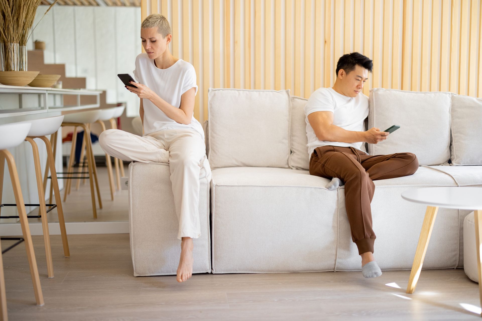 Two partners sitting apart on a couch, one looking at a phone