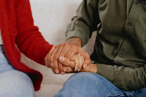 Couple sitting close on a sofa, one partner holding the other's hand
