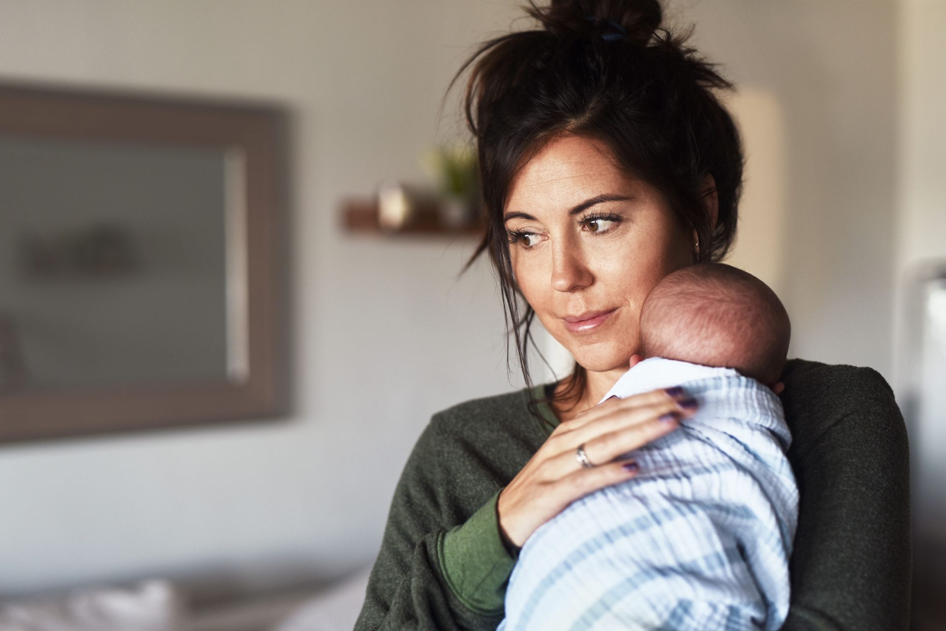 New parent holding a newborn baby, looking tired and thoughtful