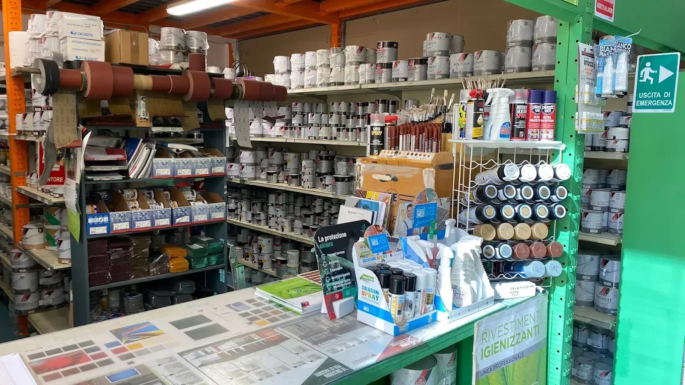 Un corridoio di un negozio al coperto, con scaffali pieni di barattoli di vernice, flaconi spray e articoli di ferramenta di vario genere.
