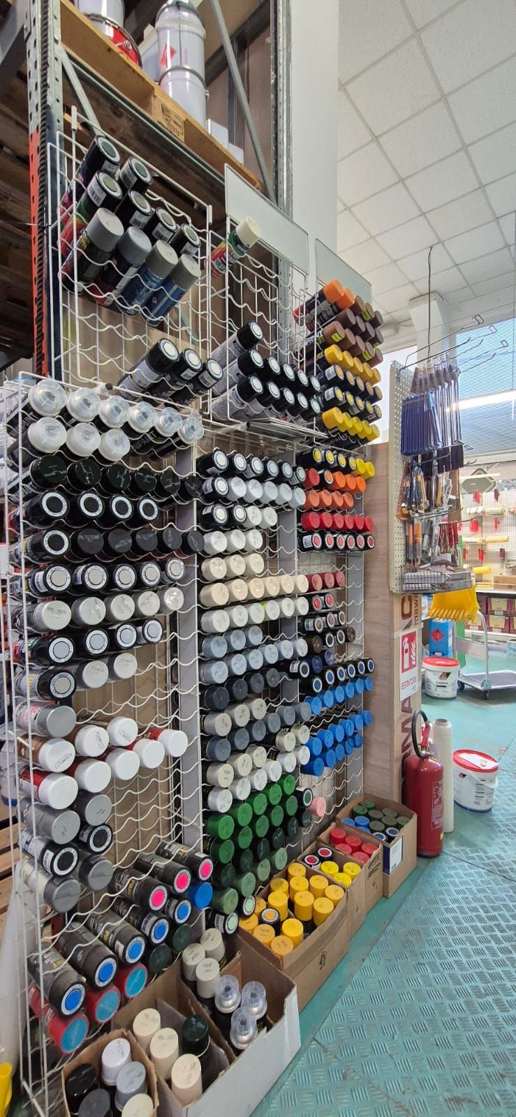 Uno scaffale espositivo in un negozio, pieno di bombolette spray di vari colori, disposte su appositi supporti.