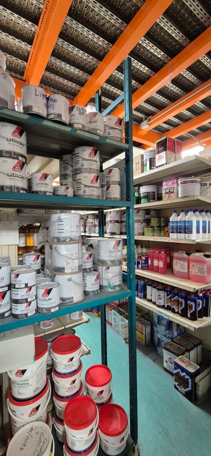 In un magazzino, gli scaffali sono pieni di barattoli di vernice bianca di vario tipo con coperchi rossi e diversi prodotti per la pulizia.