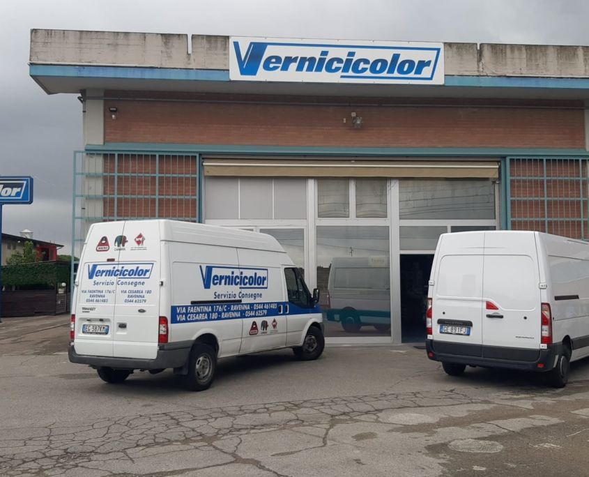 Due furgoni di servizio bianchi della Vernicicolor parcheggiati davanti a un edificio industriale in mattoni con una grande insegna aziendale.