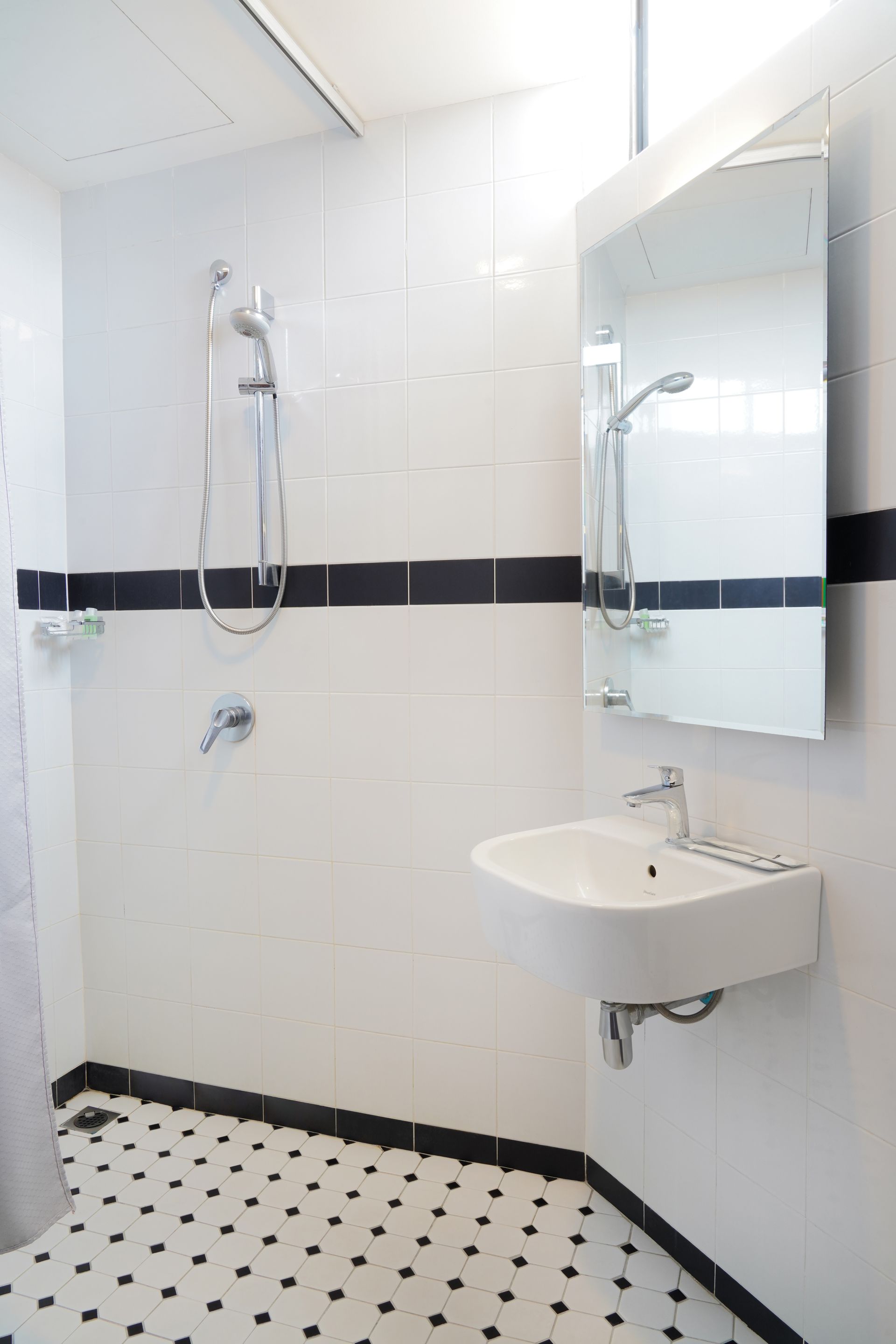 A bathroom with a sink , shower and mirror.