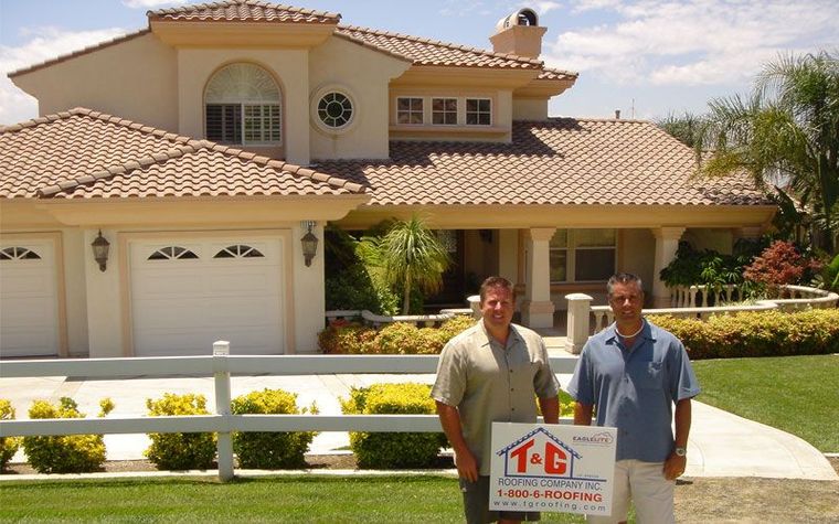 Two men standing in front of a beige house, holding a real estate sign in the front yard.