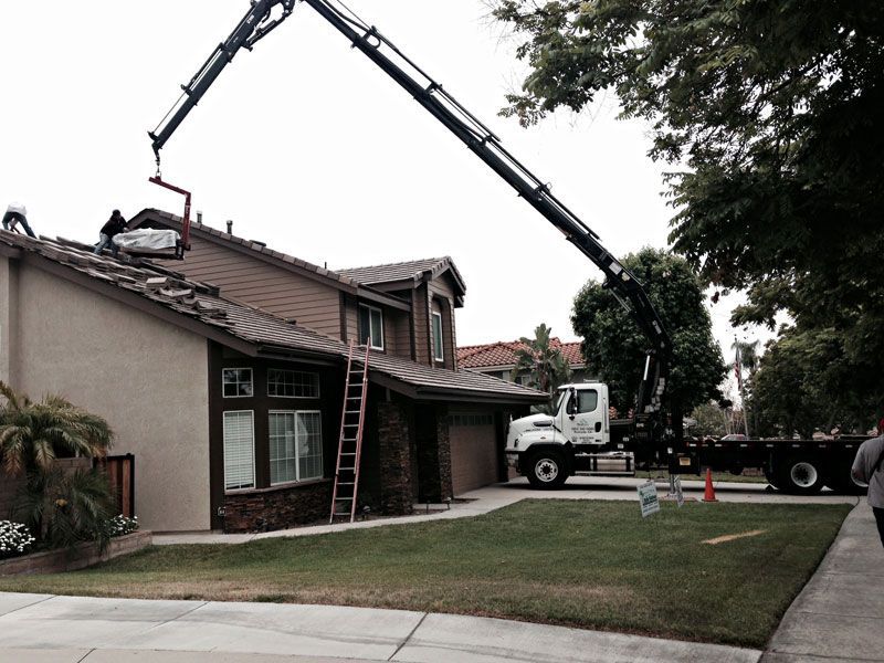 Crane lifting roofing materials onto a house during roof repair in a suburban neighborhood