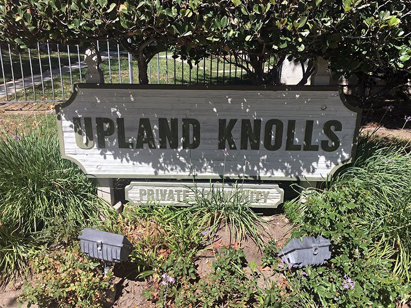 Upland Knolls entrance sign amid greenery, with a smaller private lane sign below.