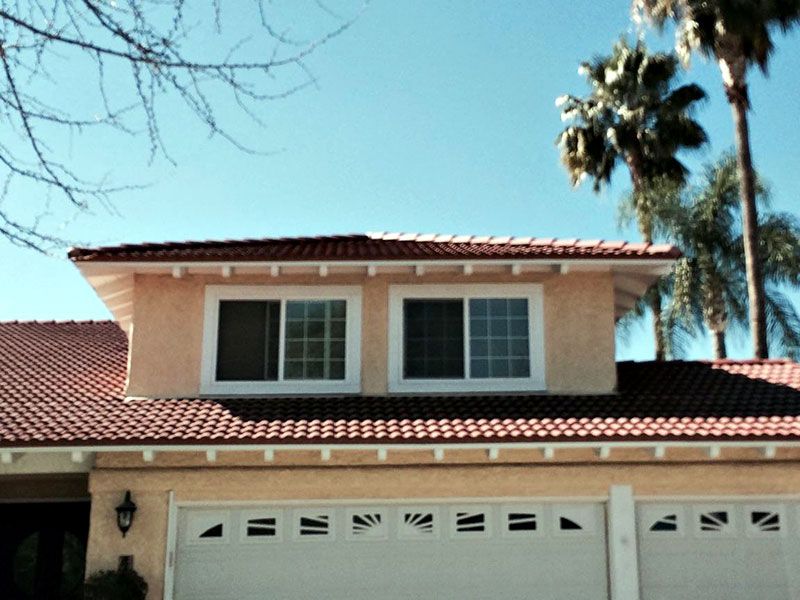 Two-story beige house with red tile roof and palm trees under a clear blue sky