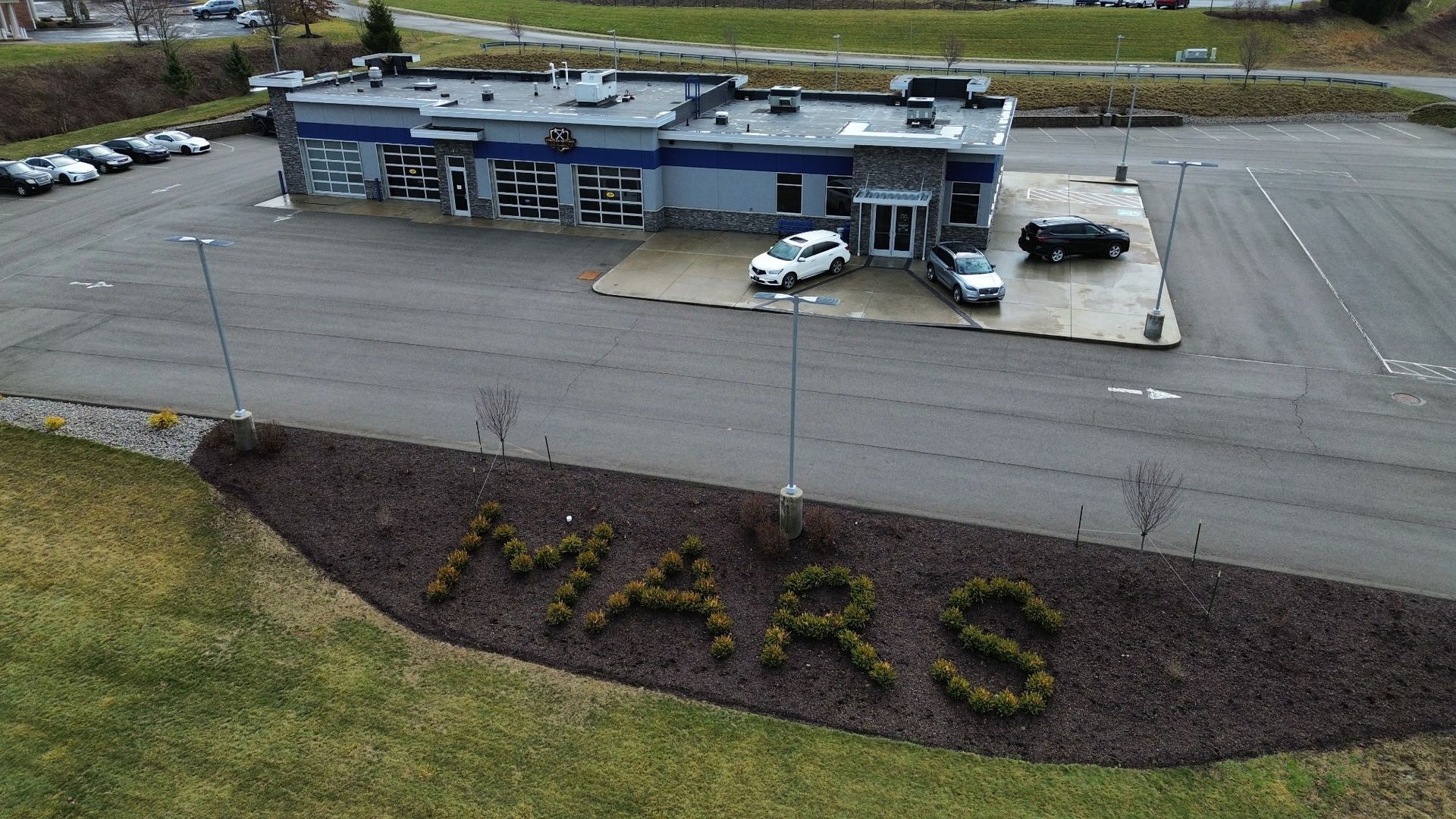 Aerial view of a low commercial building with parked cars and large “MARS” letters in landscaping. | Strother Brothers Auto Care
