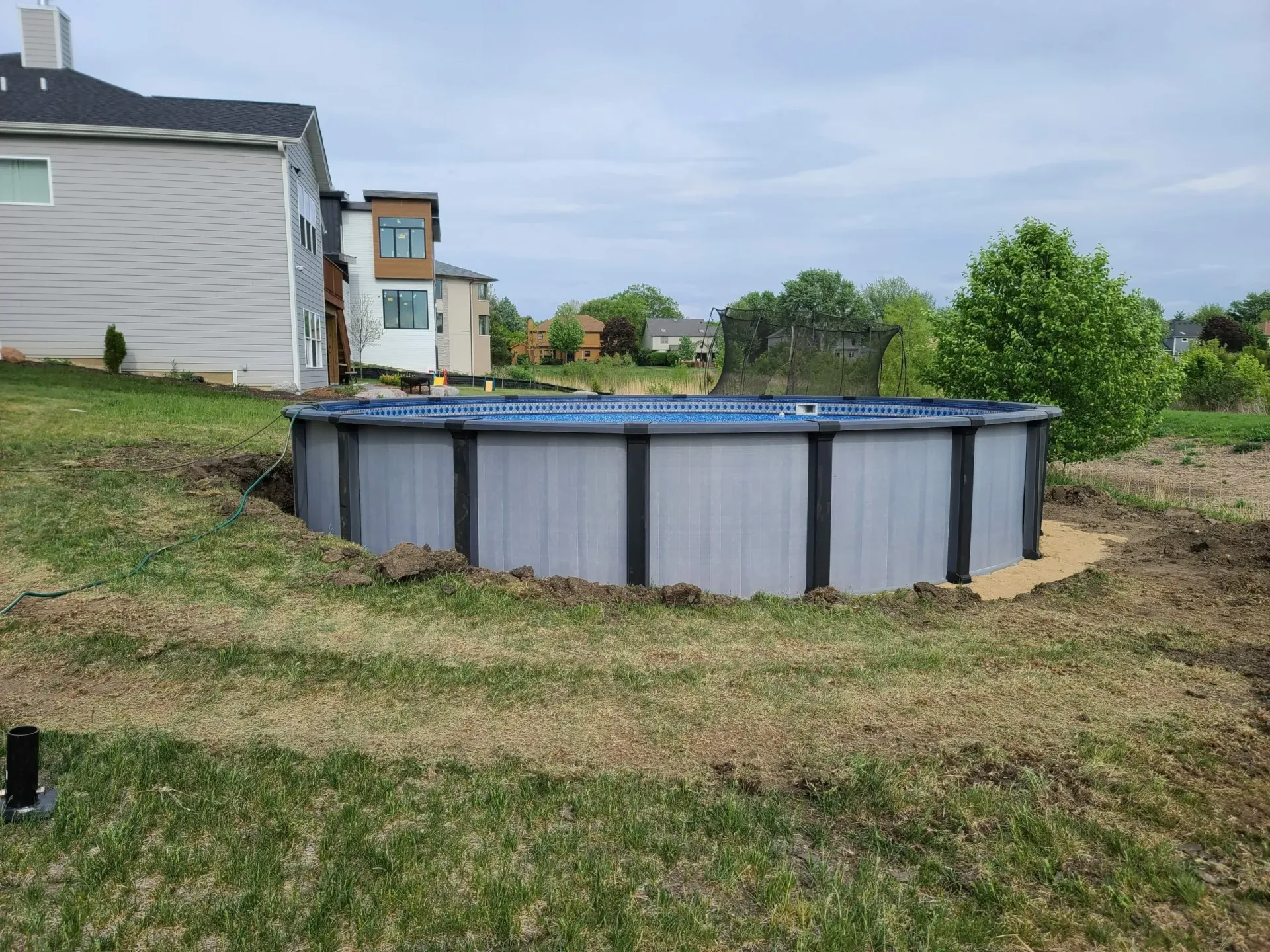 a swimming pool is sitting in the grass in front of a house .