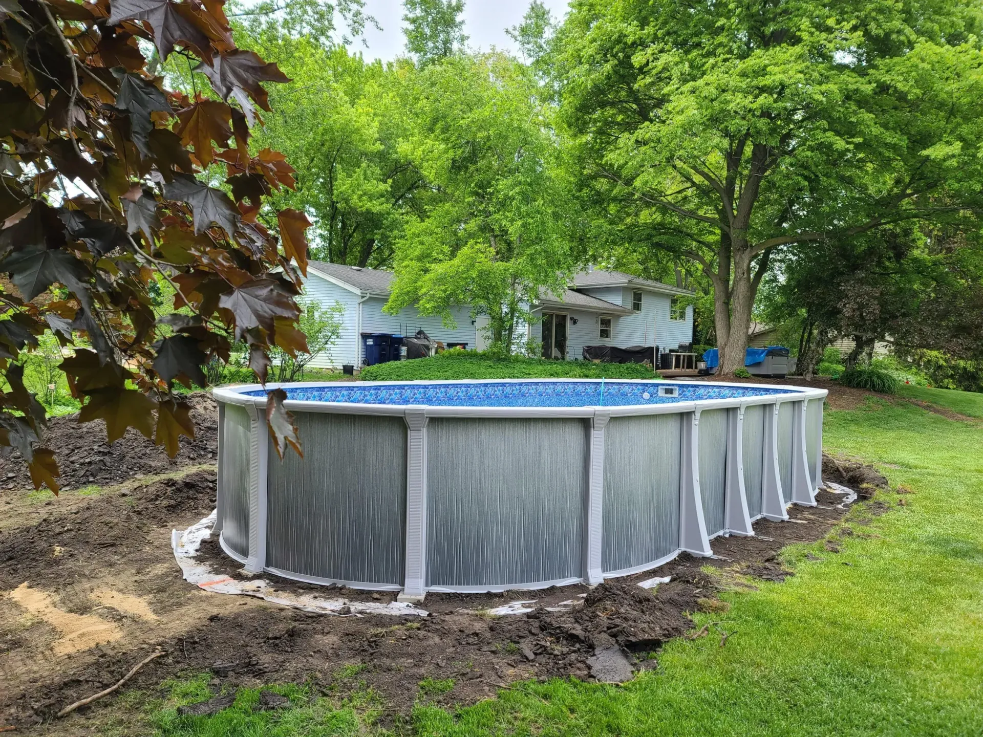 A large swimming pool is sitting in the middle of a lush green yard.