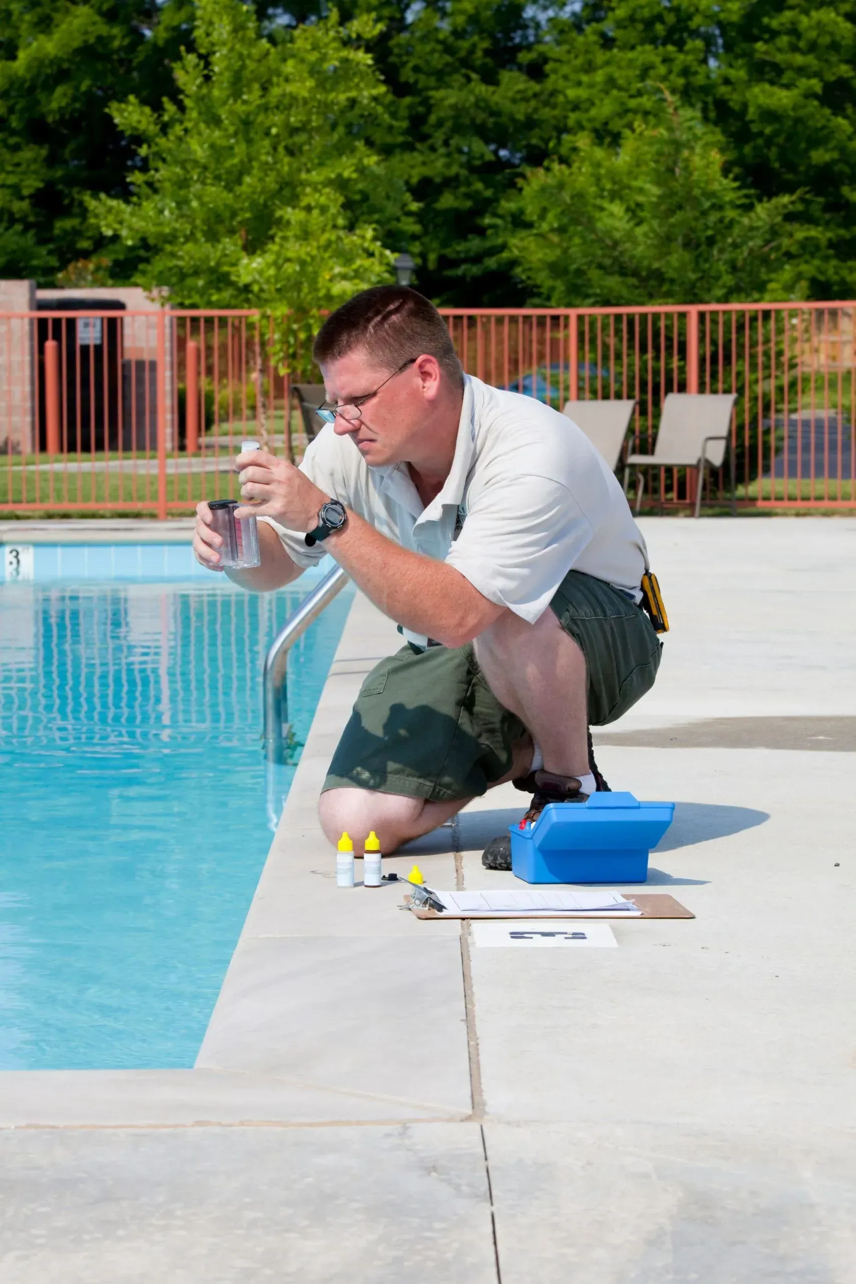 A man is kneeling next to a swimming pool looking at the water.