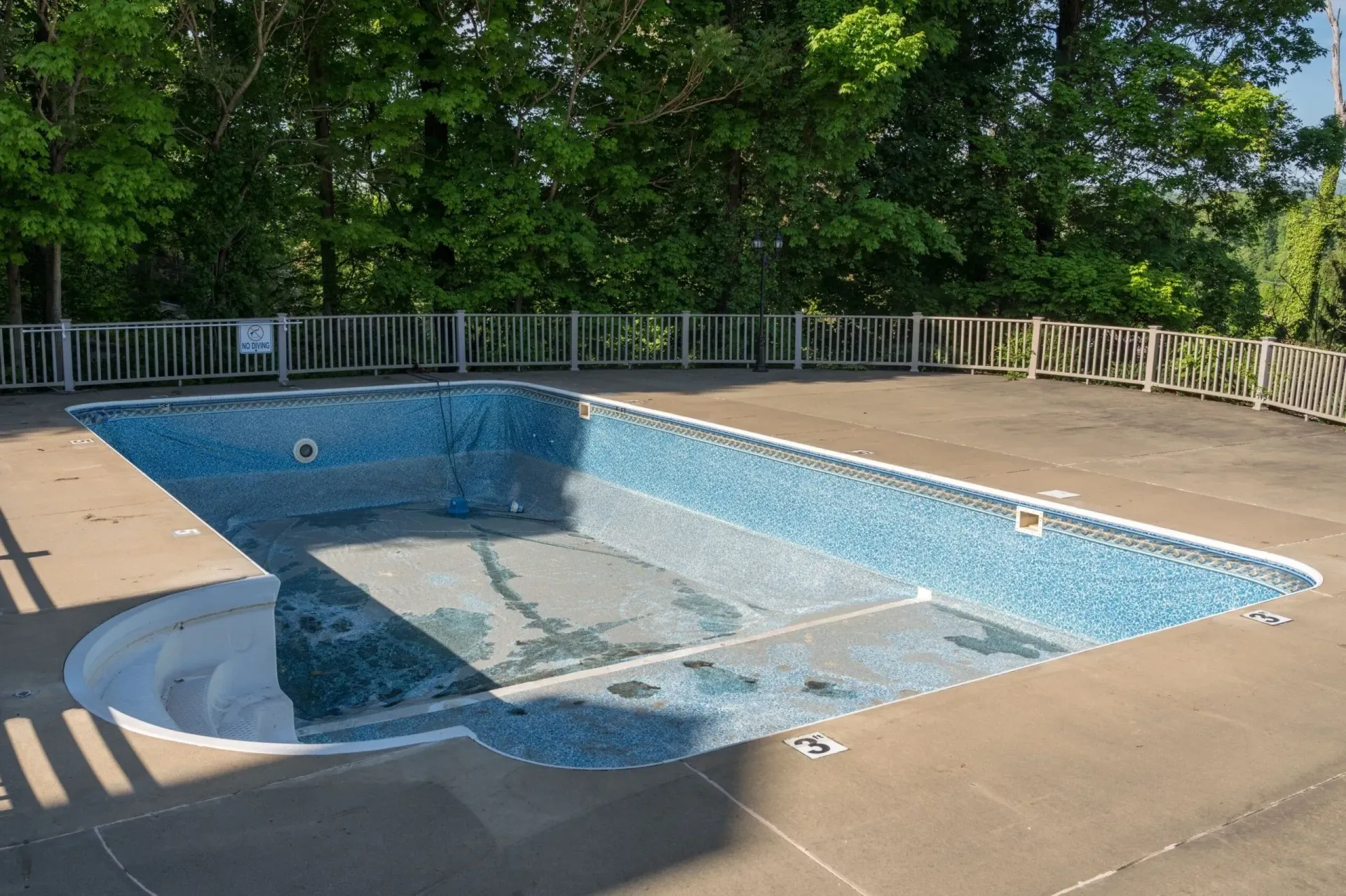 An empty swimming pool with a fence around it and trees in the background.