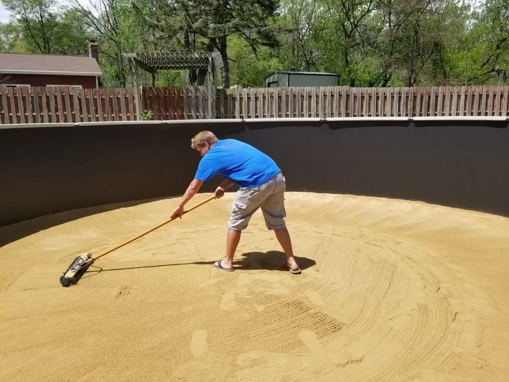 a swimming pool contractor leveling the sand bottom of an inground pool