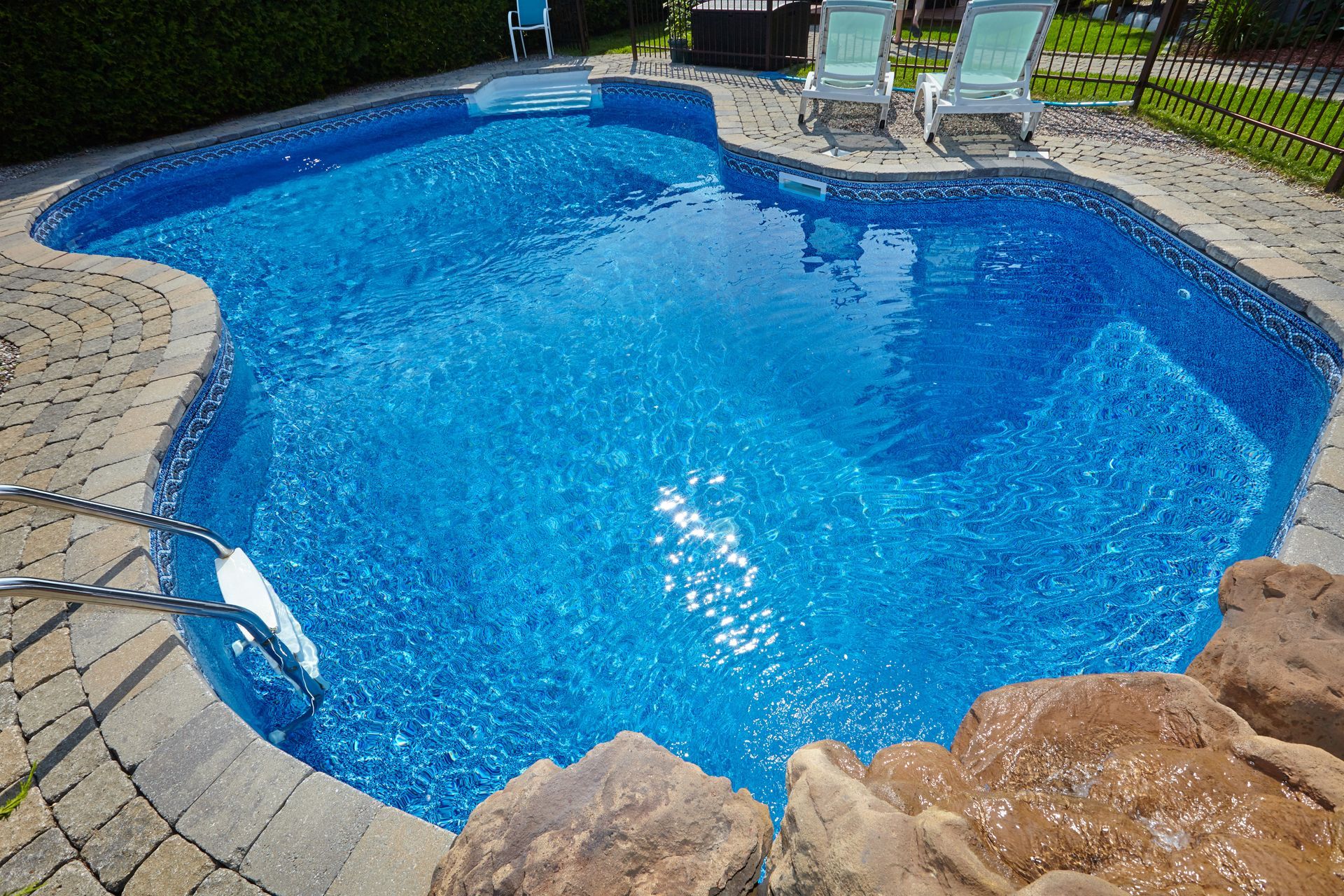 a large vinyl liner swimming pool surrounded by rocks and chairs in a backyard