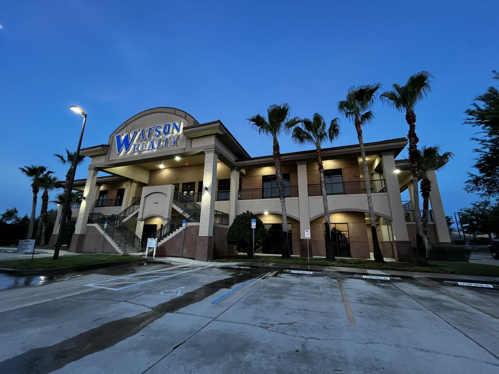 Illuminated hotel entrance at dusk with palm trees and a blue sky