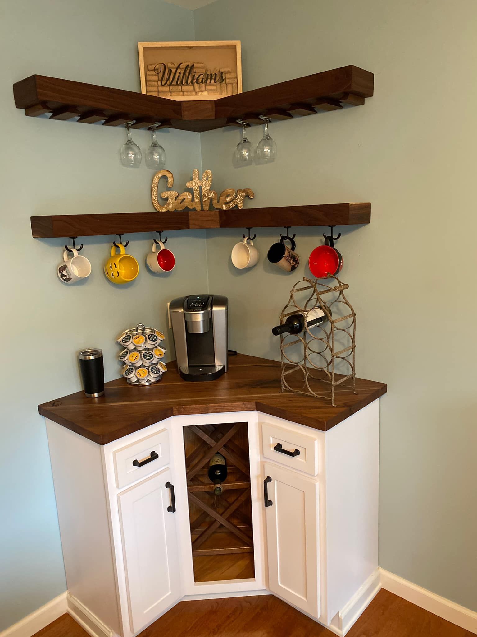 A corner bar with a wine rack , coffee maker , mugs and glasses.