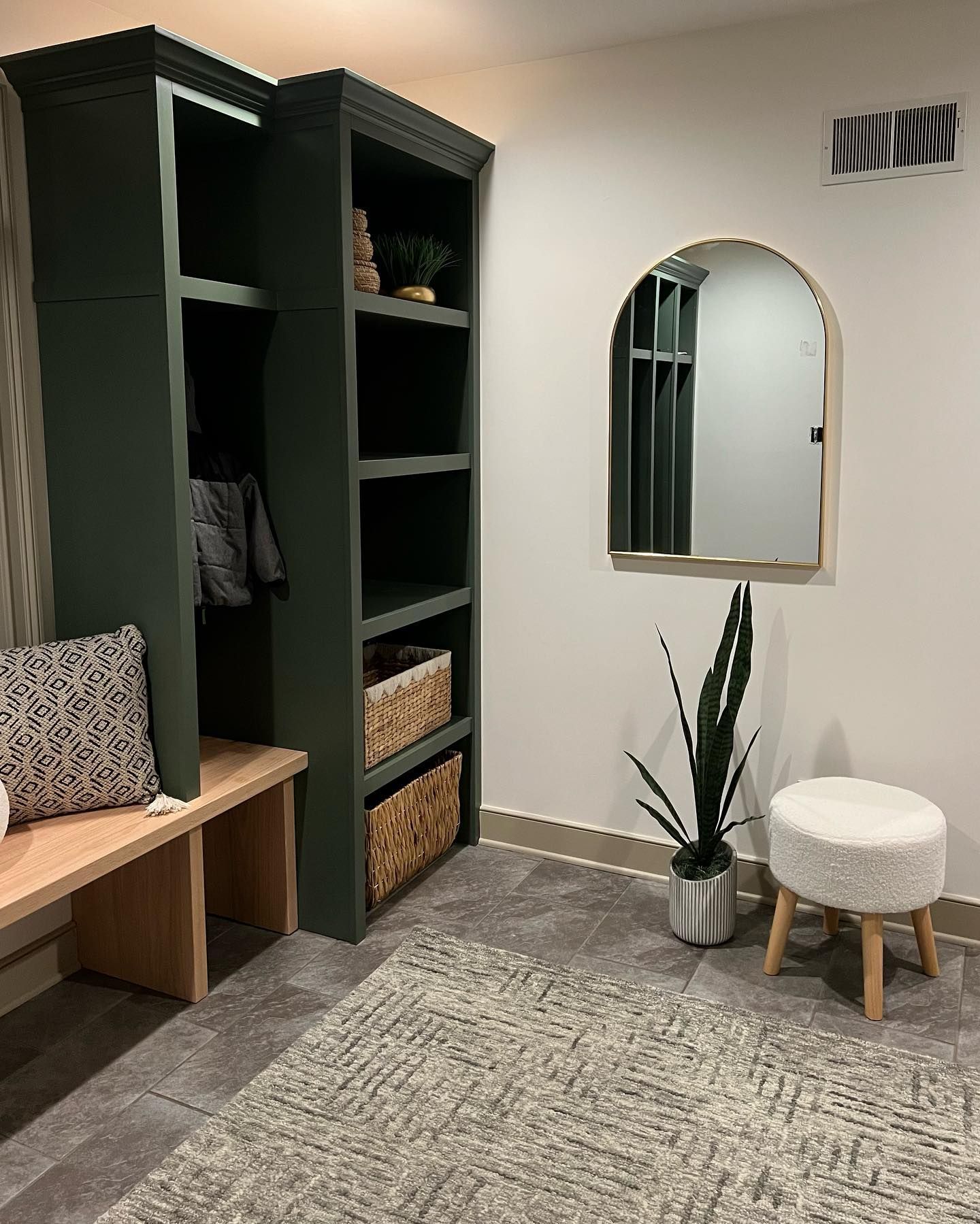 A room with a plant , a bench , a mirror and a stool.
