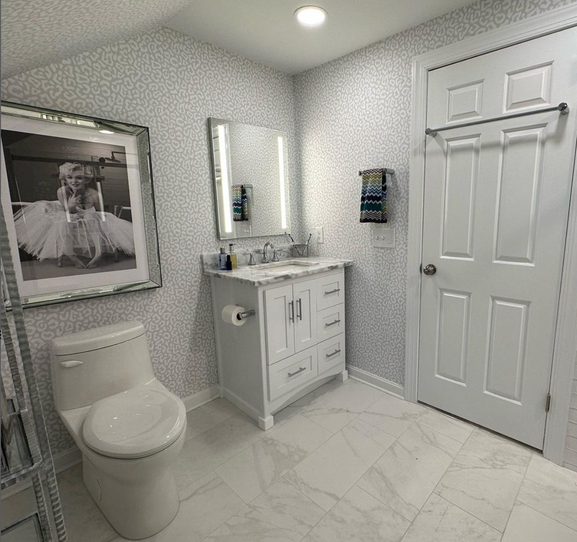 A bathroom with a toilet , sink , mirror and picture on the wall.